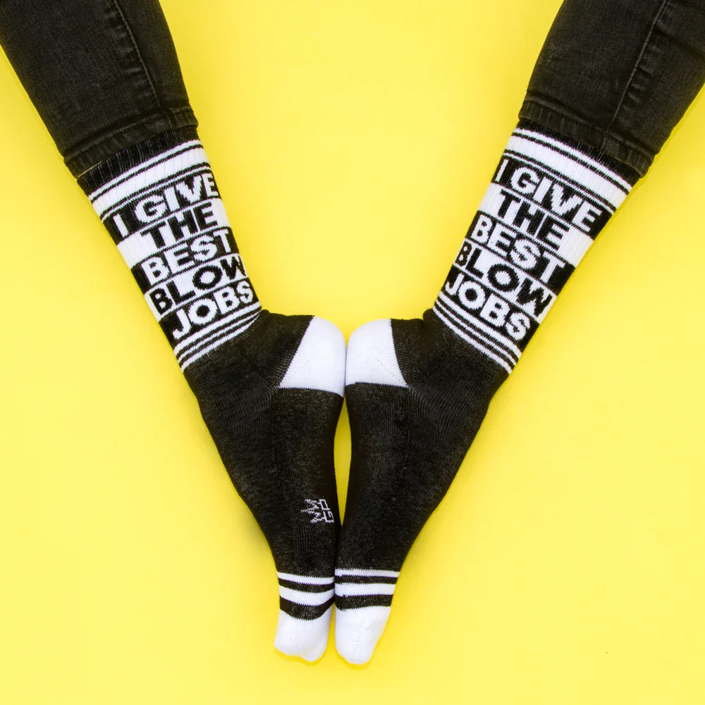 A pair of black and white crew socks that read "I give the best blow jobs" with the Gumball Poodle logo on the arch.