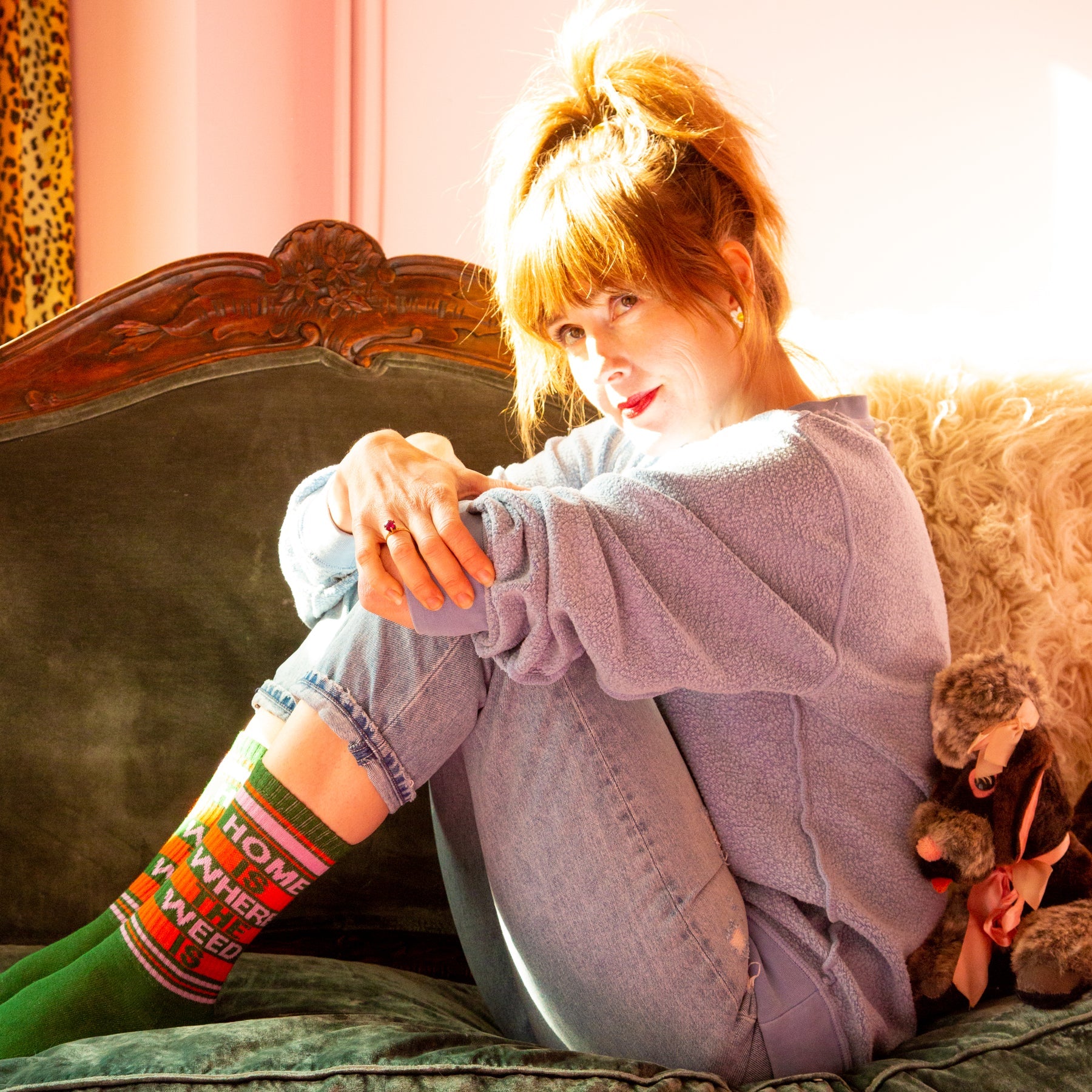 A woman wearing a pair of green, orange, and pink crew socks that read "home is where the weed is" with the Gumball Poodle logo on the arch.