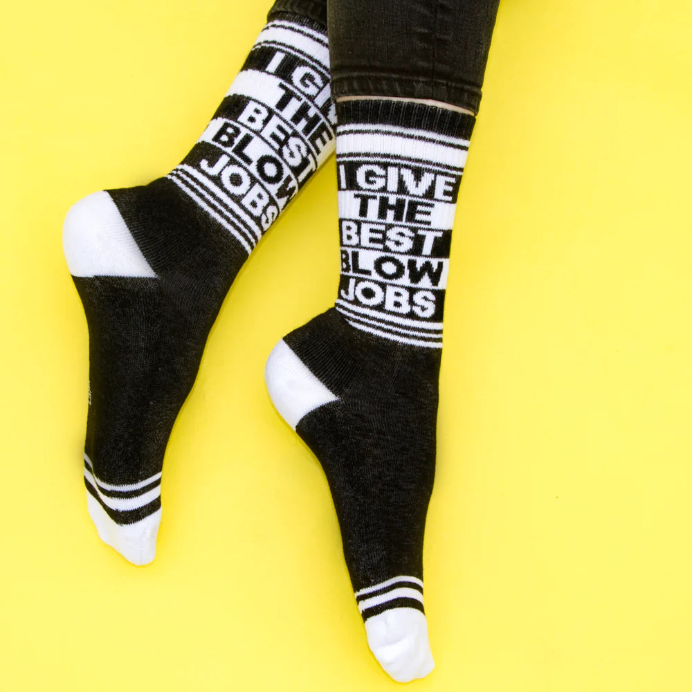 A pair of black and white crew socks that read "I give the best blow jobs" with the Gumball Poodle logo on the arch.